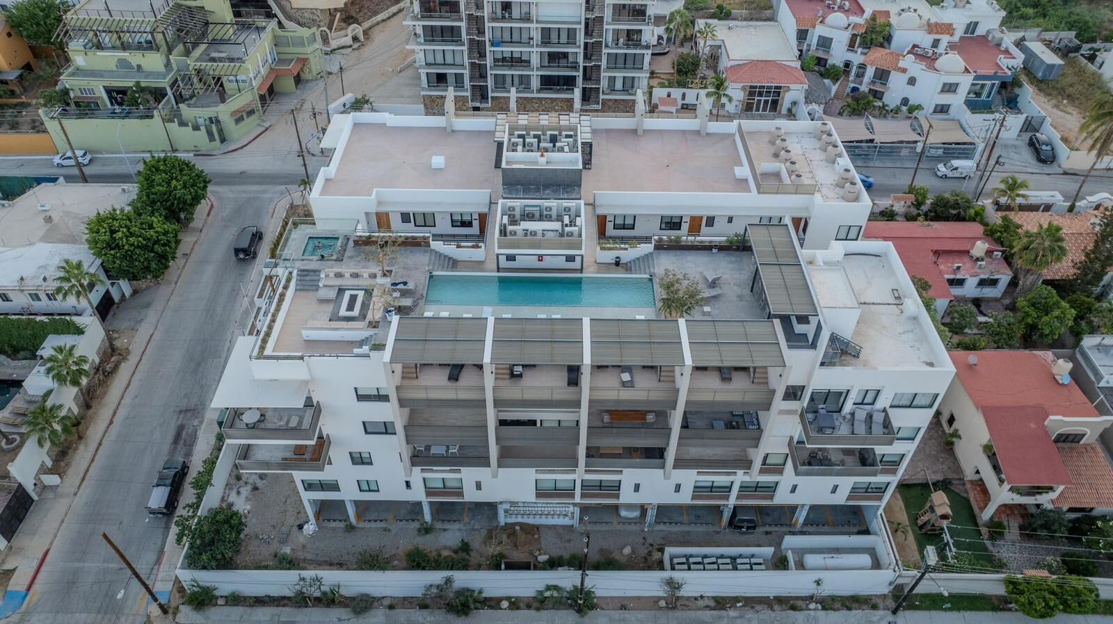 Un edificio residencial de varios pisos con piscina en la azotea, balcones y un patio central.