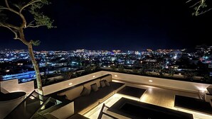 Terrassa al terrat amb una vista panoràmica de la ciutat a la nit, que inclou una zona d'estar exterior moderna i un arbre.