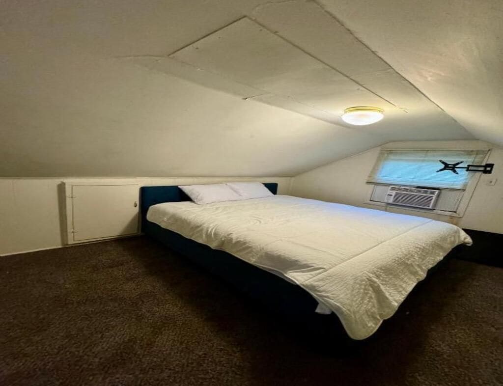 A single bed in a room with a sloped ceiling, a window with blinds, and a radiator.