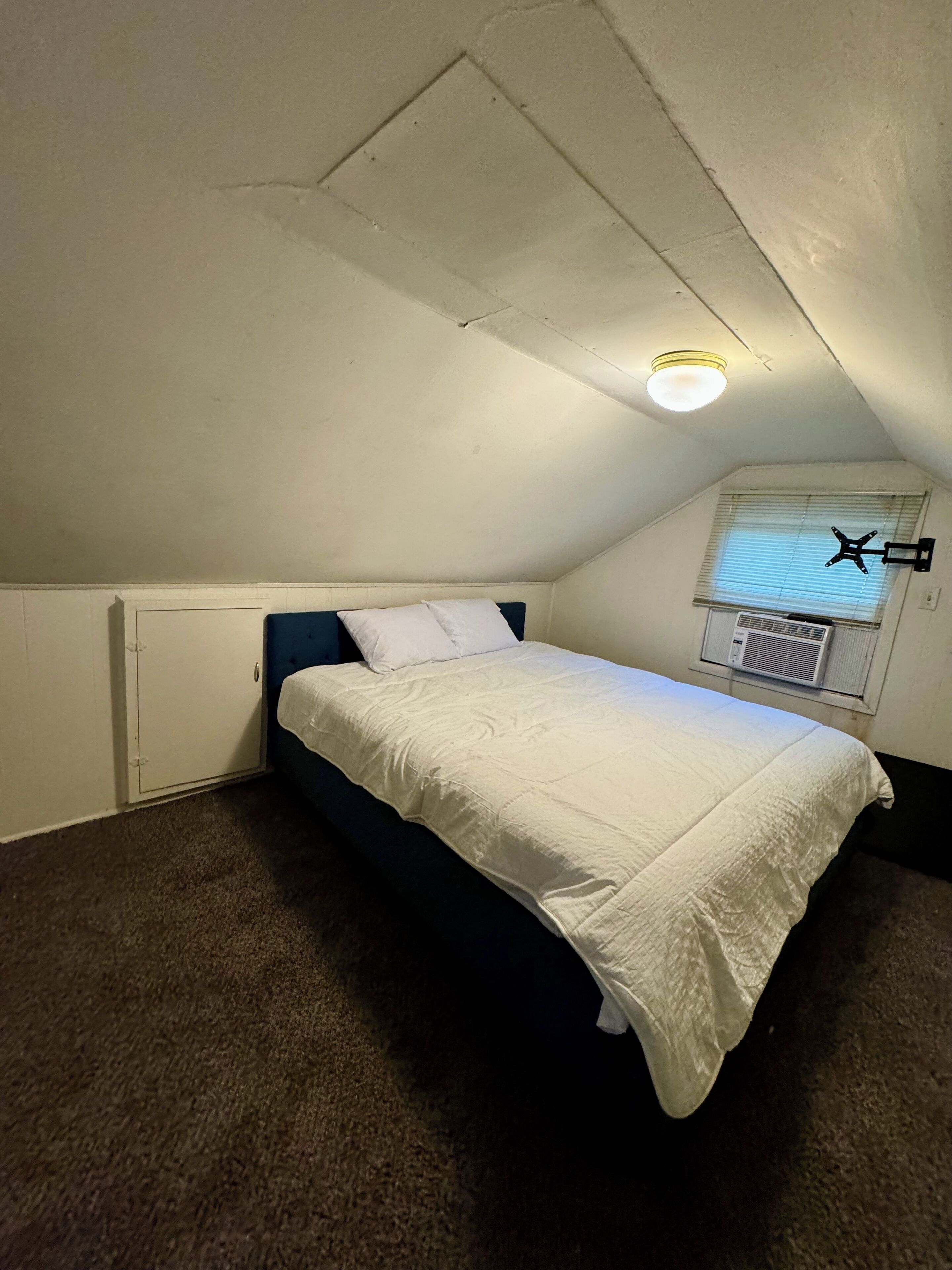 A small, dimly lit attic bedroom with a single bed, a radiator, and a window with blinds.