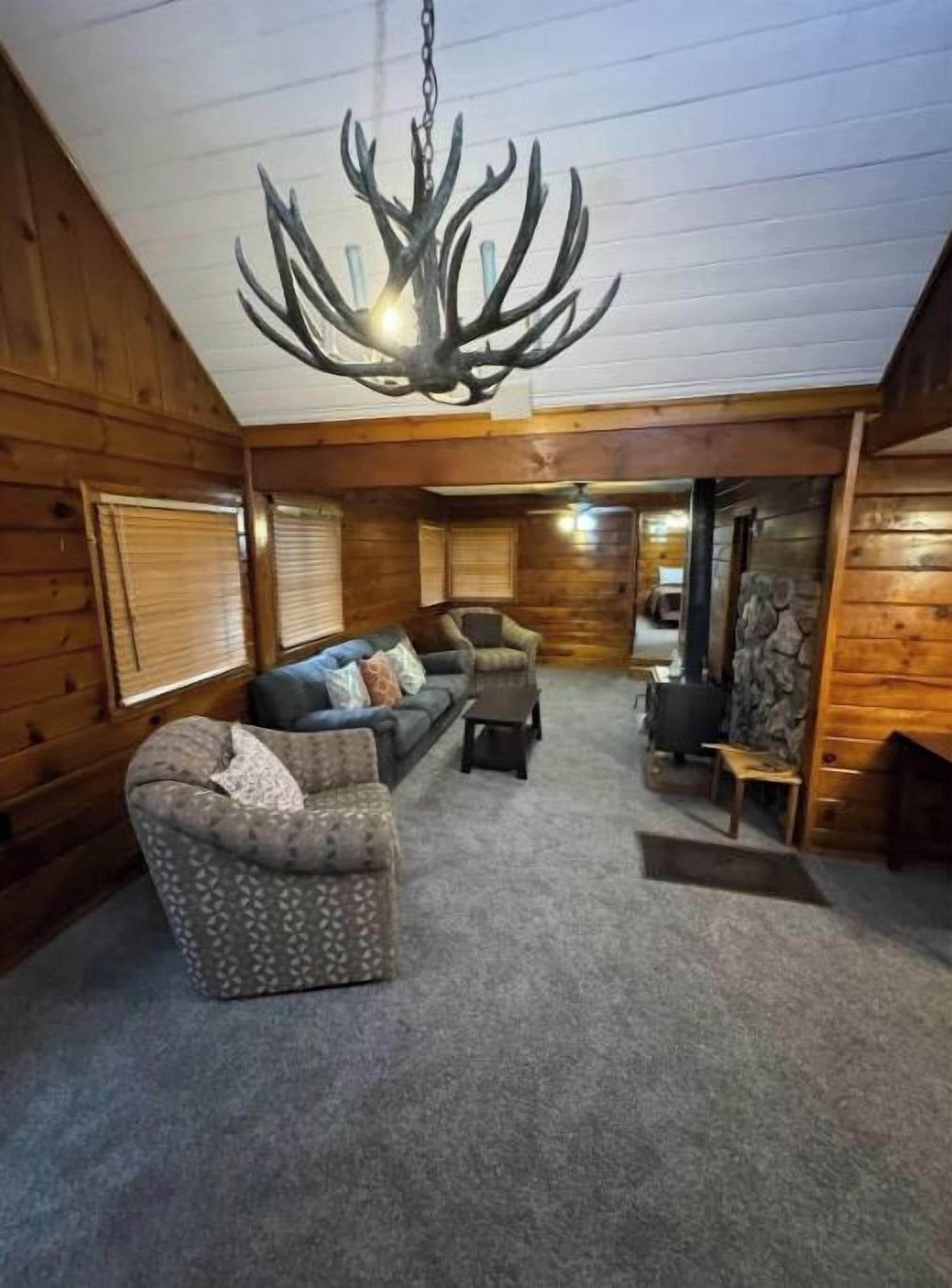 Interior d'una cabana de fusta amb un penjall, un sofà, un butacó estampat i una llar de foc.
