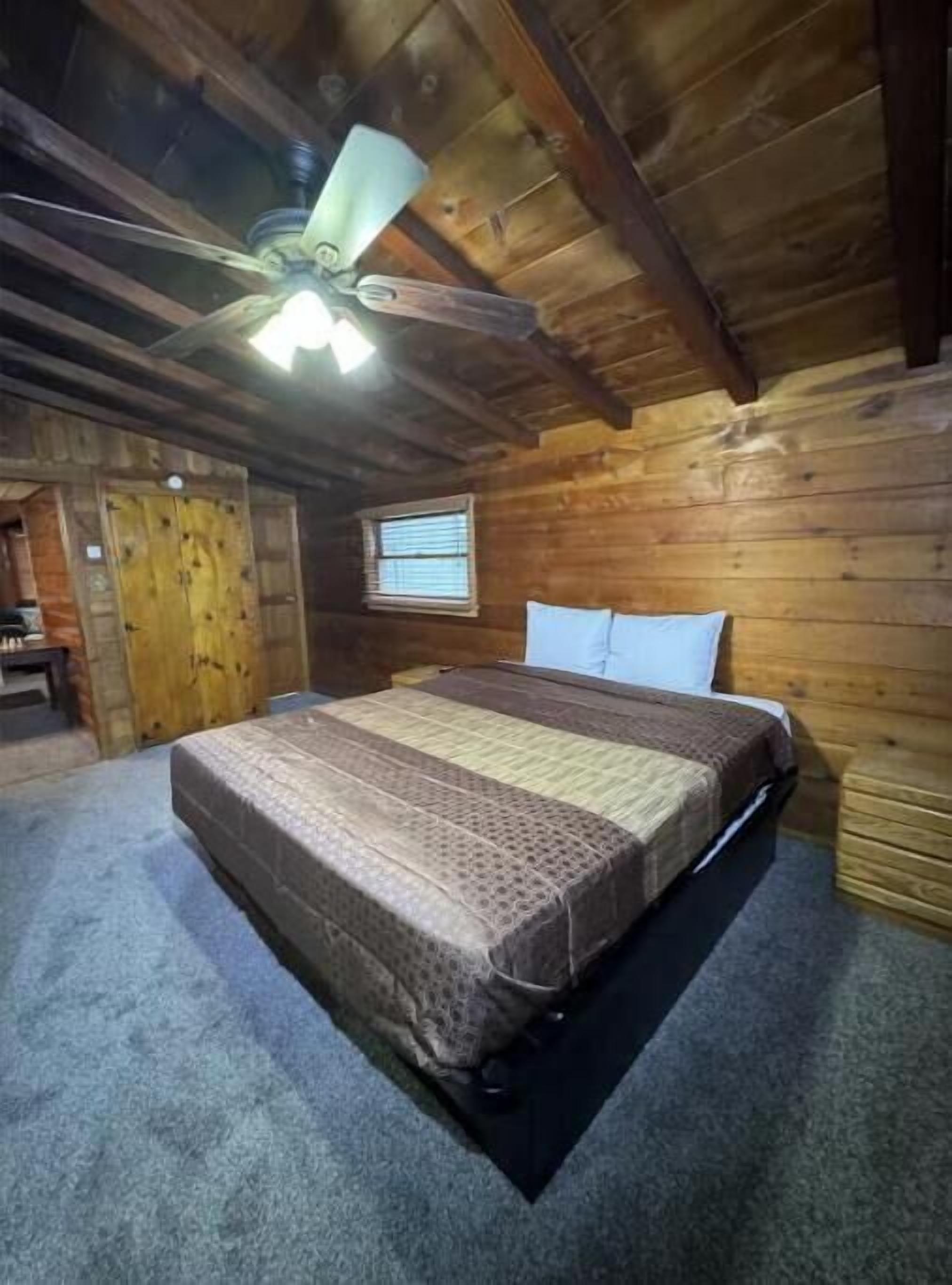 Une chambre dans une cabane en bois, avec un lit, une fenêtre et un ventilateur de plafond.