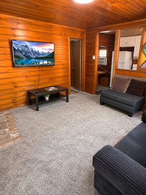 A cozy living room with a television mounted on a wooden wall, a dark sofa, and a small coffee table.