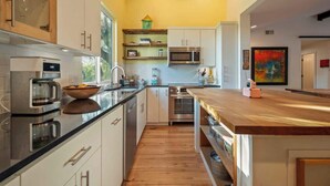 Een moderne keuken met witte kastjes, roestvrijstalen apparatuur en een houten aanrecht.
