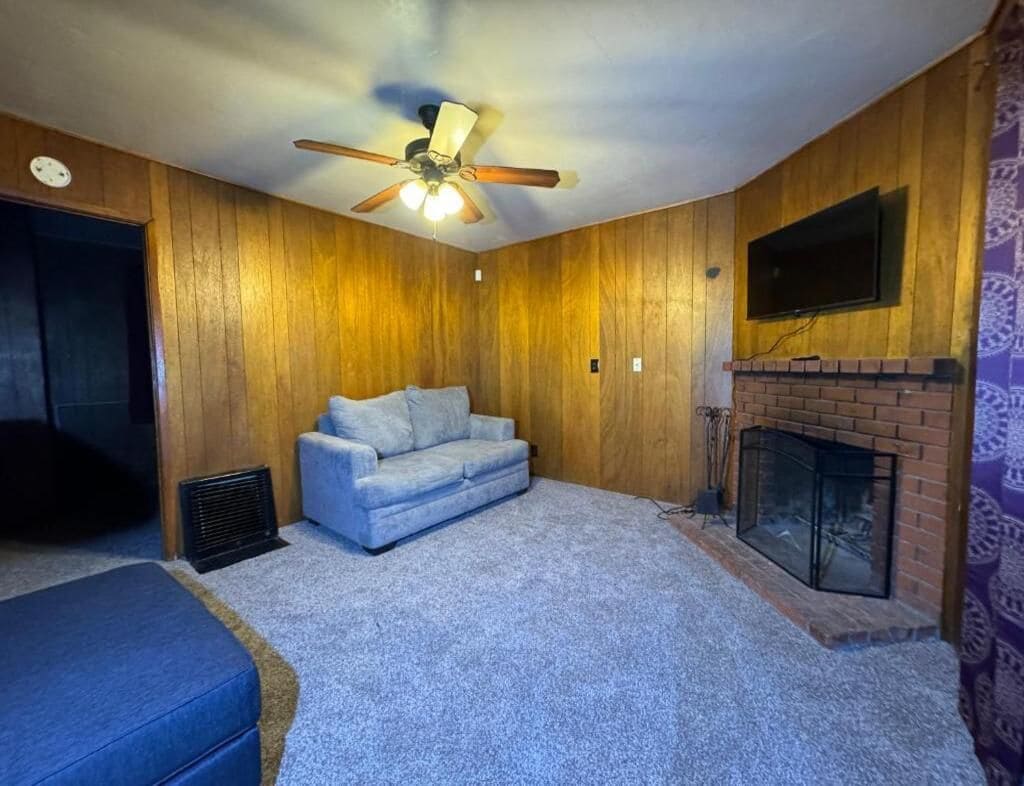 A room with a ceiling fan, a fireplace, a television mounted on the wall, and a sofa.