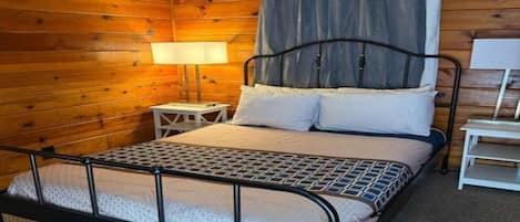 A single bed with a metal frame, a bedside table, a lamp, and a curtain.