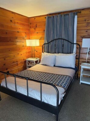 Een kamer met houten lambrisering, een bed, een nachtkastje en een lamp.