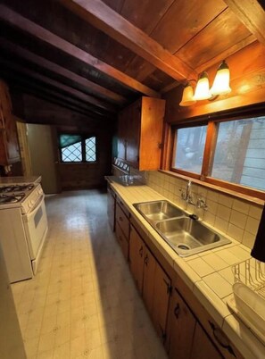 A kitchen with wooden beams, a gas stove, a sink, and a window with a view.