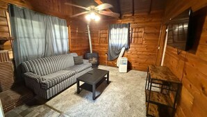 A cozy cabin interior with a checkered sofa, a coffee table, a ceiling fan, and a television mounted on the wall. - Crest Lodge Historic Mountain Inn - ArrowBear (Crestline)