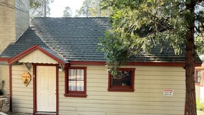 A small building with a beige exterior, a red door, and a window with a red frame. There is a sign on the wall warning about security cameras. - Crest Lodge Historic Mountain Inn - ArrowBear (Crestline)