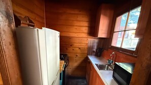 A compact kitchen with wooden walls, a refrigerator, a stove, a sink, and a window. - Crest Lodge Historic Mountain Inn - ArrowBear (Crestline)