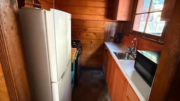 A compact kitchen with wooden walls, a refrigerator, a stove, a sink, and a window.
