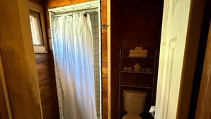A compact bathroom with a shower curtain, a toilet, and a shelf with toiletries. - Crest Lodge Historic Mountain Inn - ArrowBear (Crestline)