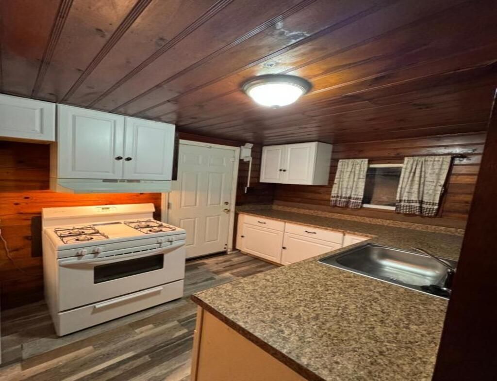 A kitchen with wooden walls, a gas stove, white cabinets, and a granite countertop.