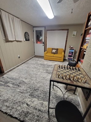 Ein Zimmer mit Schachbrett, einer Couch, einer Tür mit Milchglasfenster und einem Regal mit Kisten.