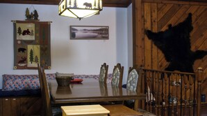 A dining area with a wooden table, chairs, and a bench. There is a decorative wall hanging with animal and tree motifs. - Loon Lodge on Bear Lake (Bear Lake)