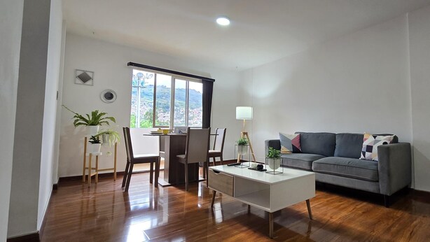 A modern living room with a dining area, a grey sofa, and a small table with a lamp.