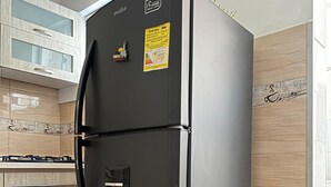 A black refrigerator with a water dispenser, a stove, and an oven in a kitchen with wooden cabinets and a tiled backsplash.