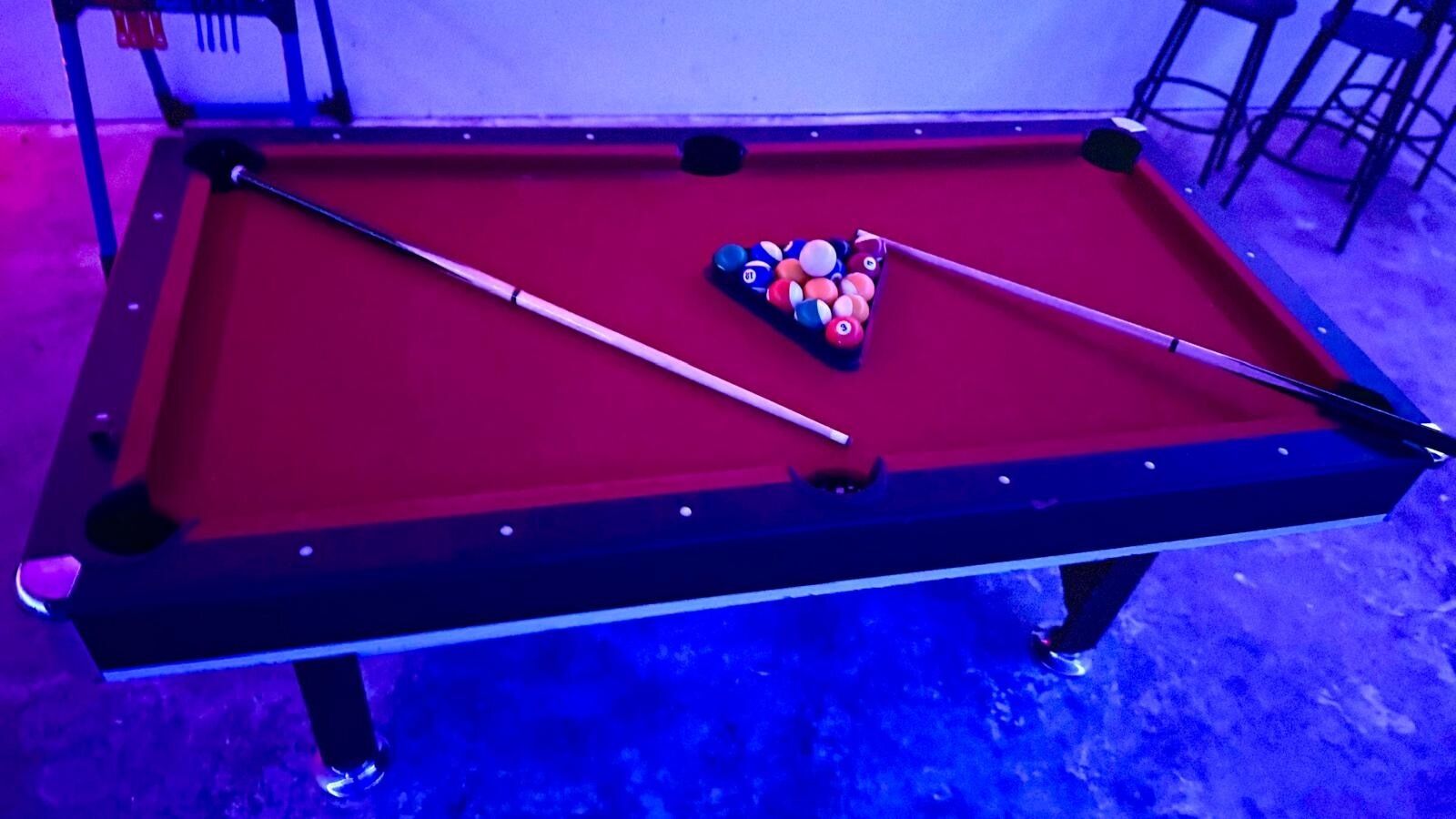 Un tavolo da biliardo con un telo rosso, due stecche e una serie di palle da biliardo.
