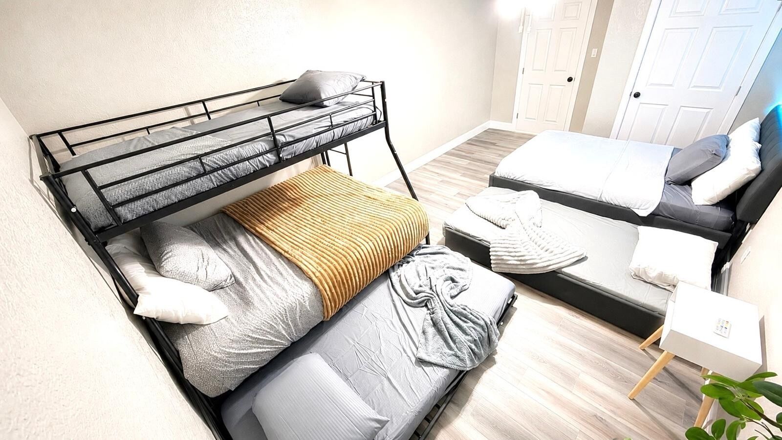 A room with a bunk bed, a sofa bed, a bedside table, and a door.