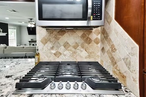 Una cocina con estufa de acero inoxidable, un microondas encima y salpicadero de azulejos.