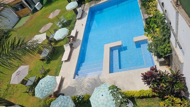 A rectangular swimming pool with a tiled edge, surrounded by a grassy area with several lounge chairs and umbrellas. - PACHA RODEO (Pachacamac)