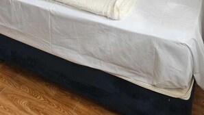 A neatly made bed with white linens, a rolled-up towel, and a remote control on a nightstand beside it. - PACHA RODEO (Pachacamac)