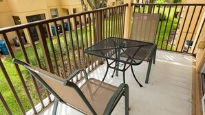 A balcony with a glass table and metal chairs, surrounded by a metal railing.