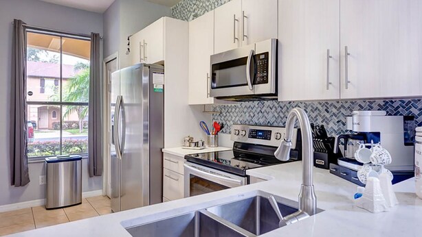A modern kitchen with stainless steel appliances, white cabinetry, and a large window providing a view of the outside.