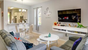A modern living room with a grey sofa, a white coffee table, and a flat-screen TV mounted on the wall.