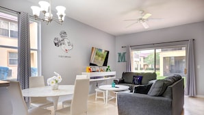 A modern living room with a grey sofa, white dining table, and a ceiling fan.