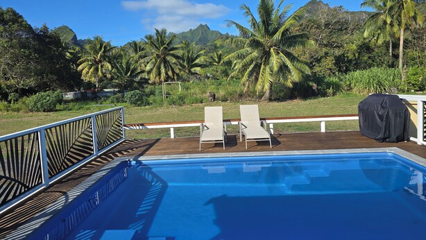 Una piscina con un pontile di legno, poltrone relax e vista su palme e montagne.
