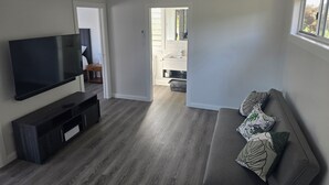 Un soggiorno moderno con televisore a schermo piatto, pavimento in legno scuro, divano grigio con cuscini fantasia e ventilatore a soffitto.