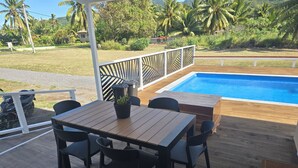 Una terrazza in legno con piscina, circondata da un recinto bianco e palme.