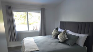 Una camera da letto con un letto grande, tende grigie e una finestra vista sul verde.