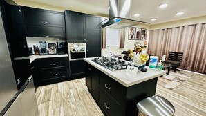 A modern kitchen with black cabinets, a central island, a gas stove, and a coffee maker. - Brooklyn Loft  (Sosúa)