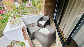A balcony with wicker furniture, a small table, and a planter with white pebbles and red flowers. - Brooklyn Loft  (Sosúa)