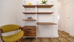 Une pièce avec un mur blanc, une chaise en bois, une bibliothèque remplie de livres et d’objets décoratifs, et un sol à motifs.