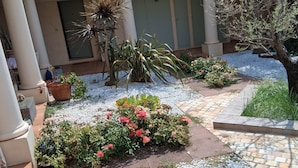 En gårdsplads med grussti, plantekasser og et lille blomsterbed.