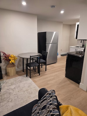 A modern kitchen with a stainless steel refrigerator, a dining area with a round table and chairs, and a small island with a sink. - FemMac's Place (Moncton)