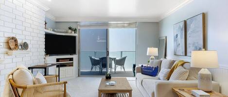 Un salon moderne avec un téléviseur, un canapé, une table basse et un balcon équipé de chaises.