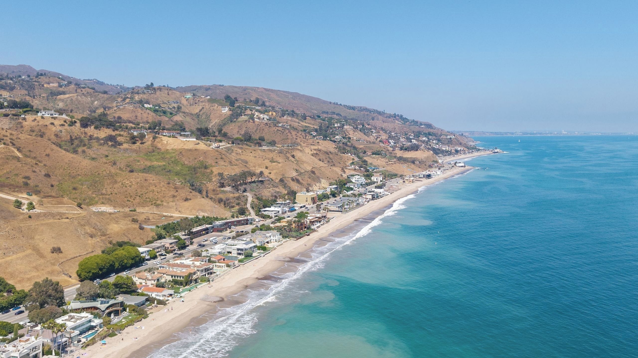 A coastal town with a beach, houses, and hills.