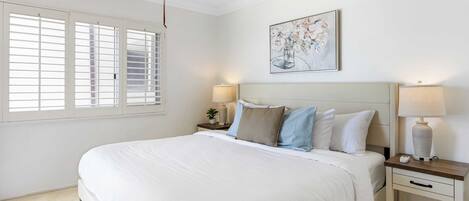 A bedroom with a large bed, two bedside tables with lamps, a ceiling fan, and a window with blinds.