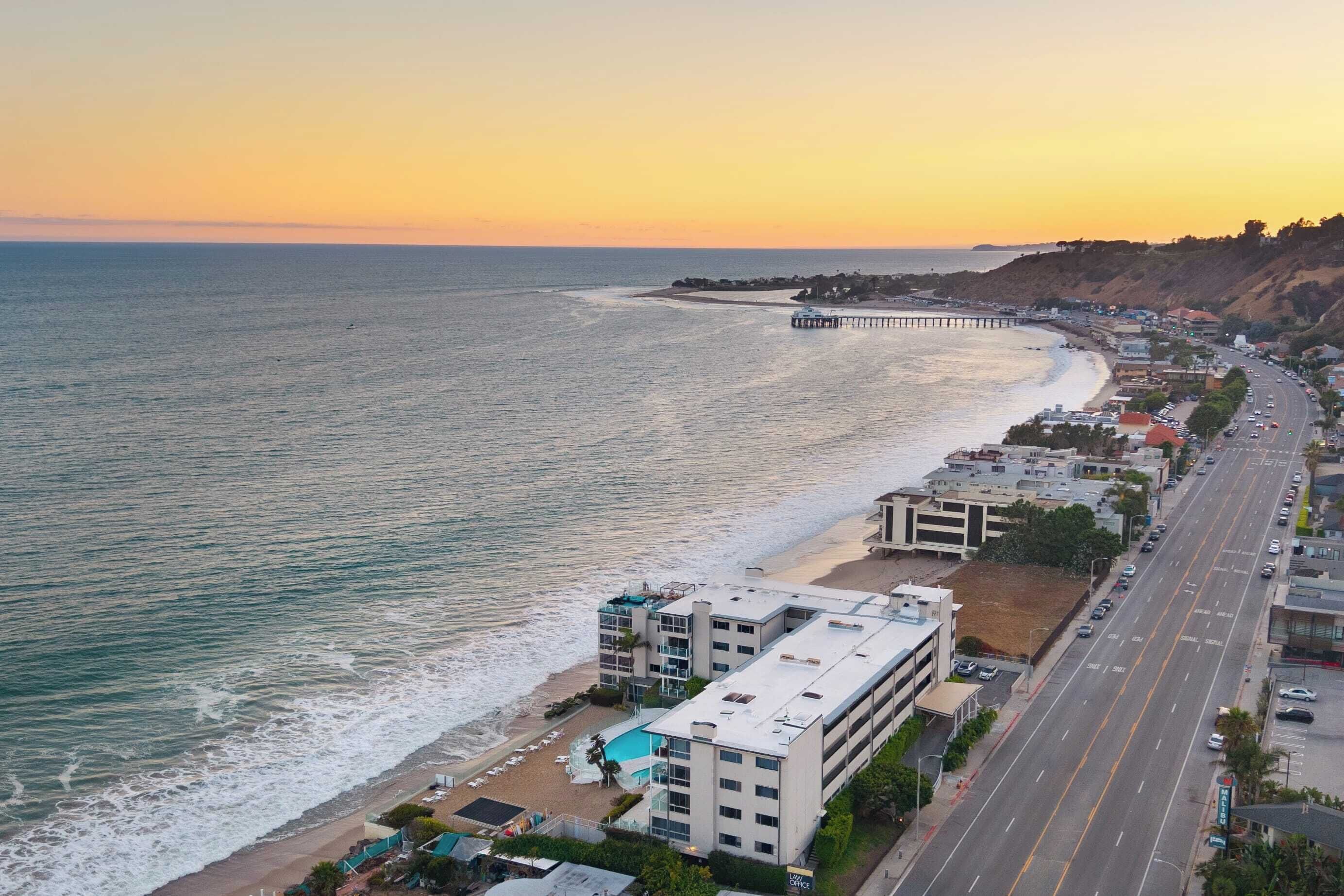 A coastal cityscape with a beach, a pier, and a multi-story hotel with a pool.
