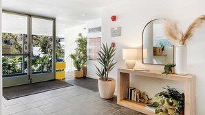 A modern hotel lobby with a large glass door leading to a parking area, a wooden console table with a mirror, and several potted plants. - Oceanfront Gem w/ Balcony, Pool, Hot Tub & Carbon Beach Access Bluewater Haven by Avantstay (Malibu)