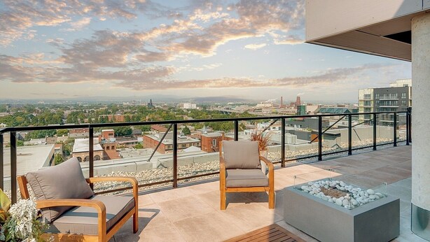Un balcón con dos sillas de madera, una chimenea pequeña y vistas a la ciudad.