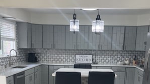 A modern kitchen with grey cabinets, a tiled backsplash, and two black bar stools. - Charming 4-bedroom house with AC in Gallup (Gallup)