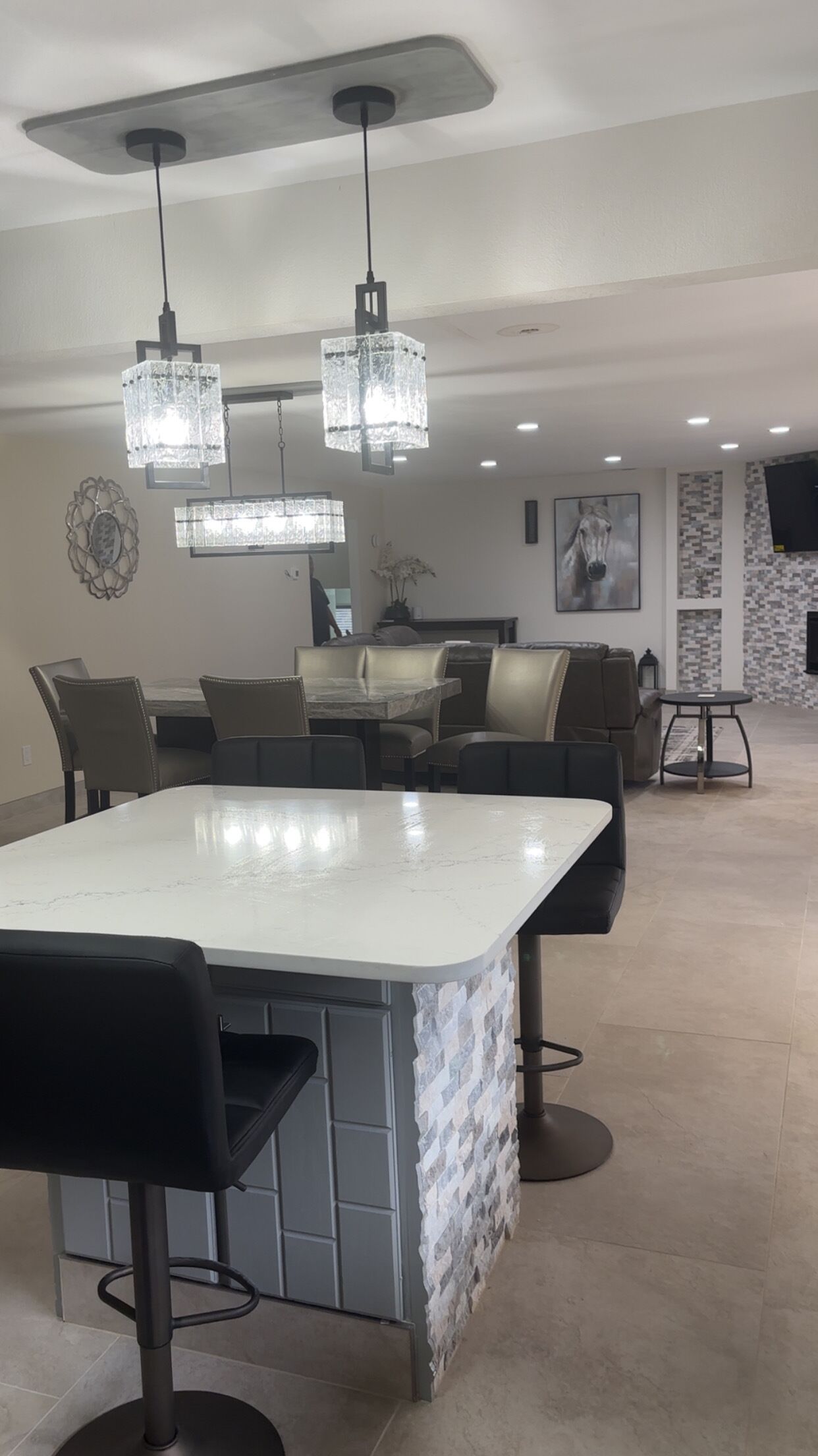 A modern kitchen with a central island, bar stools, pendant lighting, and a dining area with leather seating.