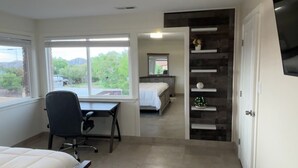 A bedroom with a bed, a desk, and a chair. There is a window providing a view of greenery outside. - Charming 4-bedroom house with AC in Gallup (Gallup)
