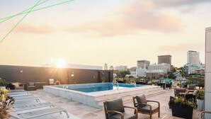 A rooftop pool area with a city skyline view, lounge chairs, and a small table.